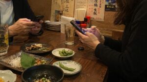 居酒屋でリラックスしながらスマートフォンを操作する男女
